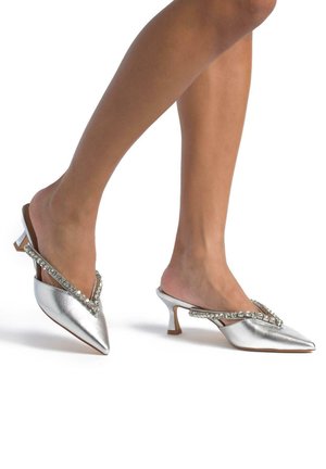 Mule metallici argento con punta affusolata, decorati con una rifinitura di strass lungo l'apertura a forma di V e un piccolo tacco robusto.