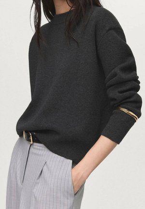 Dark gray sweater with a round neckline and cuffed sleeves, paired with light gray pinstriped trousers and a black belt. Gold accent detail on sleeve.