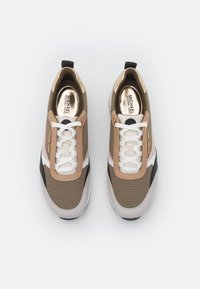 Baskets beiges et marron avec un col rembourré, des lacets blancs et des accents métalliques. Composées d'un mélange de tissu et de caoutchouc.