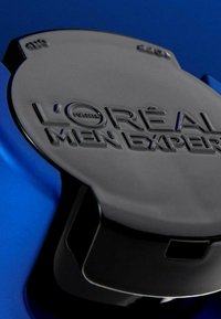 Capuchon en plastique noir avec le logo en relief "L'OREAL MEN EXPERT", sur un fond bleu brillant. Texture lisse, bords arrondis.