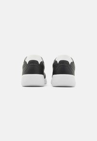 Black and white sneakers with a smooth leather upper, white rubber sole, and embossed logo on the heel. Rounded toe and cushioned collar.