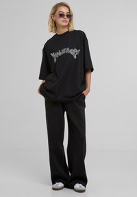 T-shirt nera oversize con dettagli in strass, abbinata a pantaloni neri larghi e sneakers bianche. Tessuto morbido; vestibilità rilassata.