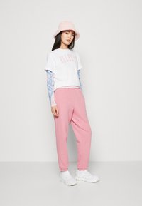 White cropped t-shirt with pink logo, layered over a light blue long-sleeve shirt. Pink joggers and a fluffy pink bucket hat, paired with white sneakers.
