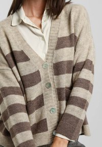 Cardigan beige con strisce marroni, realizzato in morbido maglione, con scollo a V, polsini a costine e tre grandi bottoni. Sottile texture e vestibilità rilassata.