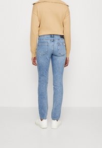 Ljusblå skinny jeans med hög midja, två bakfickor och en mörk midjedetalj, kombinerat med en beige tröja och vita sneakers.