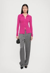Fuksia cardigan med krage og knappestolpe, paired med svart-hvitt mønstrede vide bukser og svart håndveske.