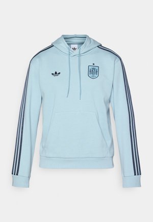 Svetlomodrá mikina s kapucňou a námorníckymi pruhmi, predná vrecko a vyšívaný španielsky erb na hrudi. Obsahuje logo Adidas na strane.