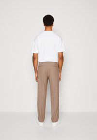 Balta īsroku T-krekls, kombinēts ar pelēcīgi brūnām biksēm un baltām sporta kurpēm. Apģērbam ir vienkāršs, tīrs dizains un brīvs piegriezums.