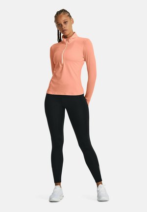 Langärmliges, mit Reißverschluss versehenes Oberteil in hellem Korall, kombiniert mit schwarzen Leggings. Das Outfit zeichnet sich durch einen schlanken Schnitt und einen glatten, dehnbaren Stoff aus.