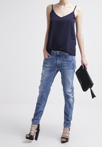 Marinsatin cami, ljusblå slitna slim-fit jeans, metalliska silverfärgade högklackade sandaler och en svart clutchväska.