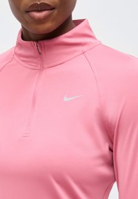 Κοντινό πλάνο ενός ατόμου που φοράει ροζ αθλητικό τοπ μακρυμάνικο με φερμουάρ στο ένα τέταρτο και λευκό λογότυπο Nike στο στήθος.