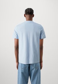 Jasnoniebieska bawełniana koszulka z krótkim rękawem i okrągłym dekoltem, widok od tyłu. W połączeniu z jasnoniebieskimi dżinsami.