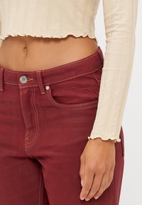 Bordeaux bomuldsbukser med en mellem-høj talje, der har sidelommer, synlige sømme og en metalknaplukning. Lys ribbet beige top.