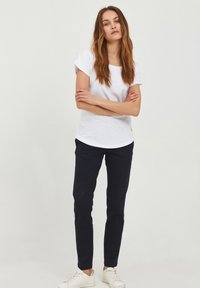 Hvit kortermet t-skjorte laget av bomull, kombinert med marineblå slim-fit bukser og hvite sneakers. Enkelt design med rund hals.