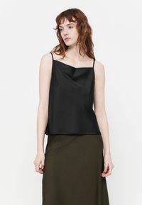 Top en satin noir avec des fines bretelles, présentant un décolleté drapé et une coupe décontractée, accompagné d'une jupe verte olive. Texture lisse.