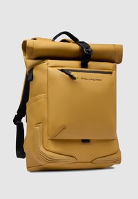 Zaino impermeabile giallo con chiusura a rotolo, tasca frontale con zip, spallacci regolabili e dettagli testurizzati. Realizzato in materiale sintetico resistente.