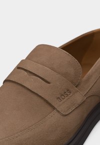 Ταν σουέτ μοκασίνι με λουράκι στην κορυφή και χαραγμένο λογότυπο "BOSS" στο πλάι κοντά στη φτέρνα.