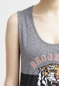 Grå ärmlös tanktop med rundad halsringning, med en tiger grafik och ordet "BROOKLYN" i orange bokstäver över bröstet.