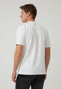Camiseta de algodón blanca con mangas cortas, cuello redondo y un corte relajado. Diseño liso sin patrones ni acentos visibles.