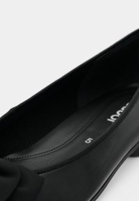 Gros plan sur une ballerine en cuir noir avec un détail de nœud et une semelle intérieure légèrement rembourrée, marquée taille 5.