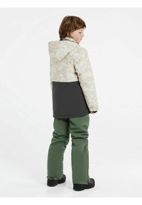 Schneejacke mit einem hellen, gemusterten oberen Bereich, dunkelgrauem Unterteil, kombiniert mit grünen Schneehosen. Verfügt über eine Kapuze und elastische Bündchen.