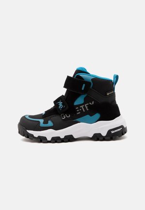 Botte de randonnée montante noire et bleue avec semelle blanche, deux bandes velcro, semelle robuste et marquage Gore-Tex imperméable sur le côté.