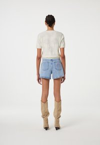 Lichtbeige korte mouw trui met bloemenpatroon, gecombineerd met blauwe denim shorts; het model draagt beige kniehoge laarzen met puntige hakken.