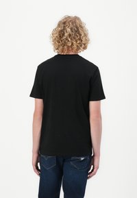 Svart bomull T-skjorte med rund hals og korte ermer, vist fra baksiden. Kombinert med mørkeblå denim jeans.