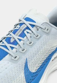 Pogled od blizu na svijetloplavu trku Nike Pegasus s plavim swooshom, bijelom mrežastom tkaninom i sivoj vezicama provučenim kroz rupice.