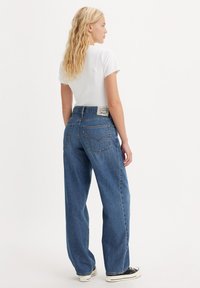 Niebieskie spodnie dżinsowe z wysokim stanem o luźnym kroju, z klasycznym pięciokomorowym wzorem oraz białą naszywką z logo na tylnym pasku.