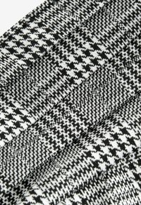 Vlněná tkanina s houndstooth vzorem v černobílém provedení. Vyznačuje se texturovaným povrchem a je složená pro vrstvený vzhled.