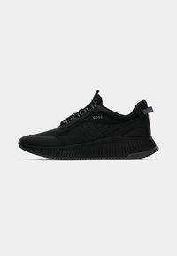 Baskets de sport noires avec une tige texturée, des accents perforés, des lacets et une semelle épaisse avec des rainures. Marque affichée sur le côté.