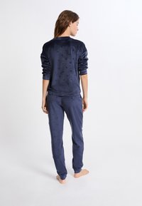 Granatowy welurowy zestaw loungewear składający się z bluzy z okrągłym dekoltem i spodni. Delikatny wzór serca oraz elastyczne mankiety w obu elementach.