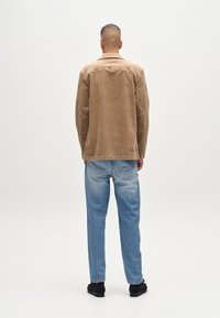 Pruunist korduroost jakist koos tekstuurse pinnaga, mis on kombineeritud helesiniste denim-püksidega. Mustad jalanõud täiendavad komplekti.
