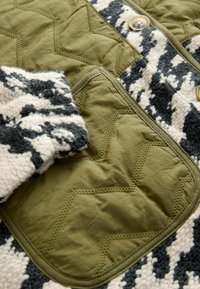 Patsitud roheline jakk, millel on tekstureeritud must-valge mustriga krae, kaks nööpi ja kantkott tekstureeritud viimistlusega.