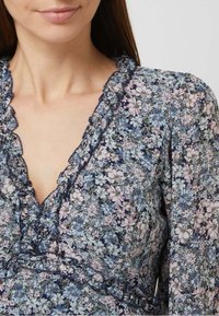 Rob e floral avec un fond marine et des fleurs roses et bleues. L'encolure et les bords des manches volantés ajoutent texture et détails.