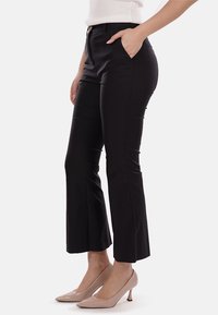 Pantaloni neri a zampa d'elefante con una consistenza liscia, vita alta e tasche laterali. Abbinati a tacchi alti nudi.