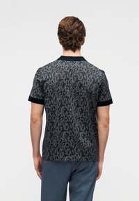 Κοντομάνικο πόλο μπλουζάκι σε σκούρο γκρι με ένα διακριτικό, περίπλοκο μοτίβο φύλλων, με μοντέρνο μαύρο γιακά και άκρες μανικιών.