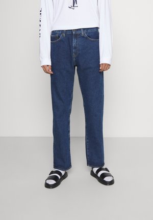 Blå denim jeans med rett benfitt, med et klassisk fem-lomme design og gule sømmer. Kombinert med svart og hvit sandaler.