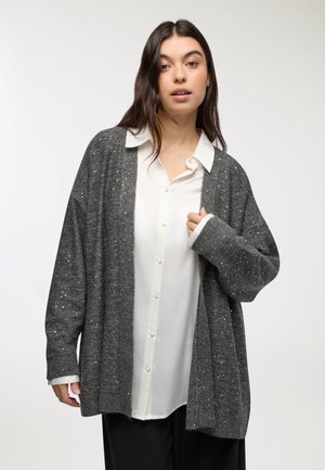 Cardigan grigio lavorato a maglia con glitter argentati, design a apertura frontale, maniche lunghe, indossato sopra una camicia bianca con bottoni. Texture morbida, vestibilità rilassata.