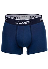 Lacoste marinblå boxershorts med en kontrasterande svart midja som har vit "LACOSTE"-text och en liten logotyp. Slät tygtextur.