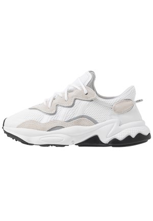 Hvid og grå atletiksneaker med en mesh-overdel, ruskindsdetaljer, bølgende designlinjer og en tekstureret sort ydersål.