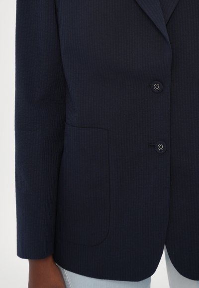 Navy blue textured blazer featuring a notch lapel, two buttons, and a single pocket on the left side. Smooth fabric with a subtle ribbed pattern.