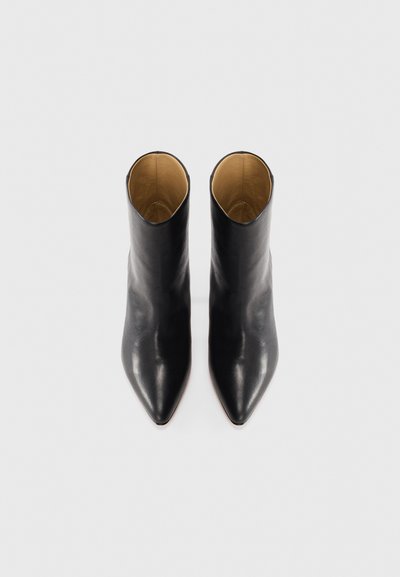 Bottes chevilles en cuir noir avec un bout pointu et une texture lisse, présentant un design minimaliste et une doublure intérieure brun clair.