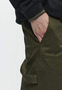 Olivgrüne Cargo-Hose mit Seitentasche, aus strapazierfähigem Material. Sichtbare Nähte und praktische Gestaltung für Funktionalität.