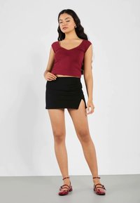 Bordo prilagođeni crop top s kap sleevima, u kombinaciji s crnom mini suknjom s bočnim prorezom. Model nosi bordo ravne cipele.