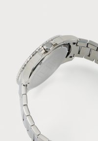 Montre en acier inoxydable argenté avec une finition polie, un boîtier rond, une couronne texturée et un bracelet à maillons, visible de côté.
