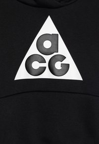 Sudadera negra con un gran logo triangular blanco que presenta las letras "acg" en tipografía negrita y redondeada negra. Textura de tela suave.