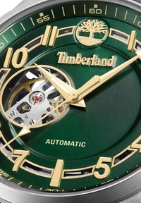 Orologio con quadrante verde e dettagli dorati, movimento automatico e meccanica interna visibile. Presenta indici delle ore prominenti e il logo del marchio.