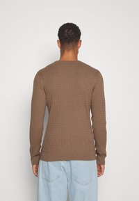 Brun ribbad tröja med långa ärmar och rund halsringning, gjord av texturerat tyg, med en åtsittande midja och ärmslut.